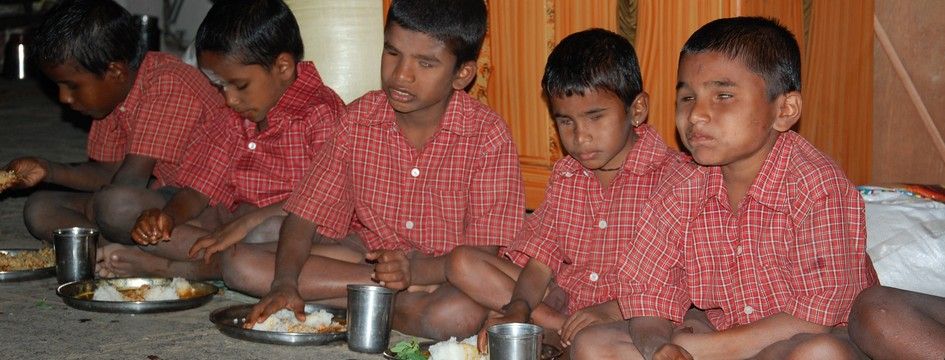 Children in school uniforms sitting on the floor and sharing a meal together.