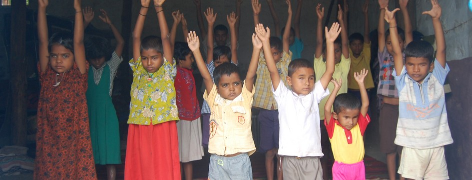 Young children standing in rows with their arms raised, practising yoga at the school.